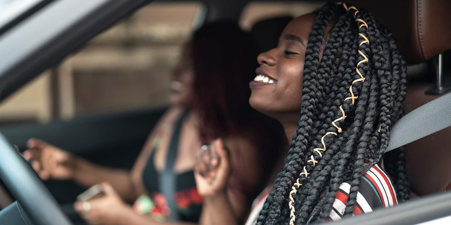 Two young women with big smiles driving in a car.