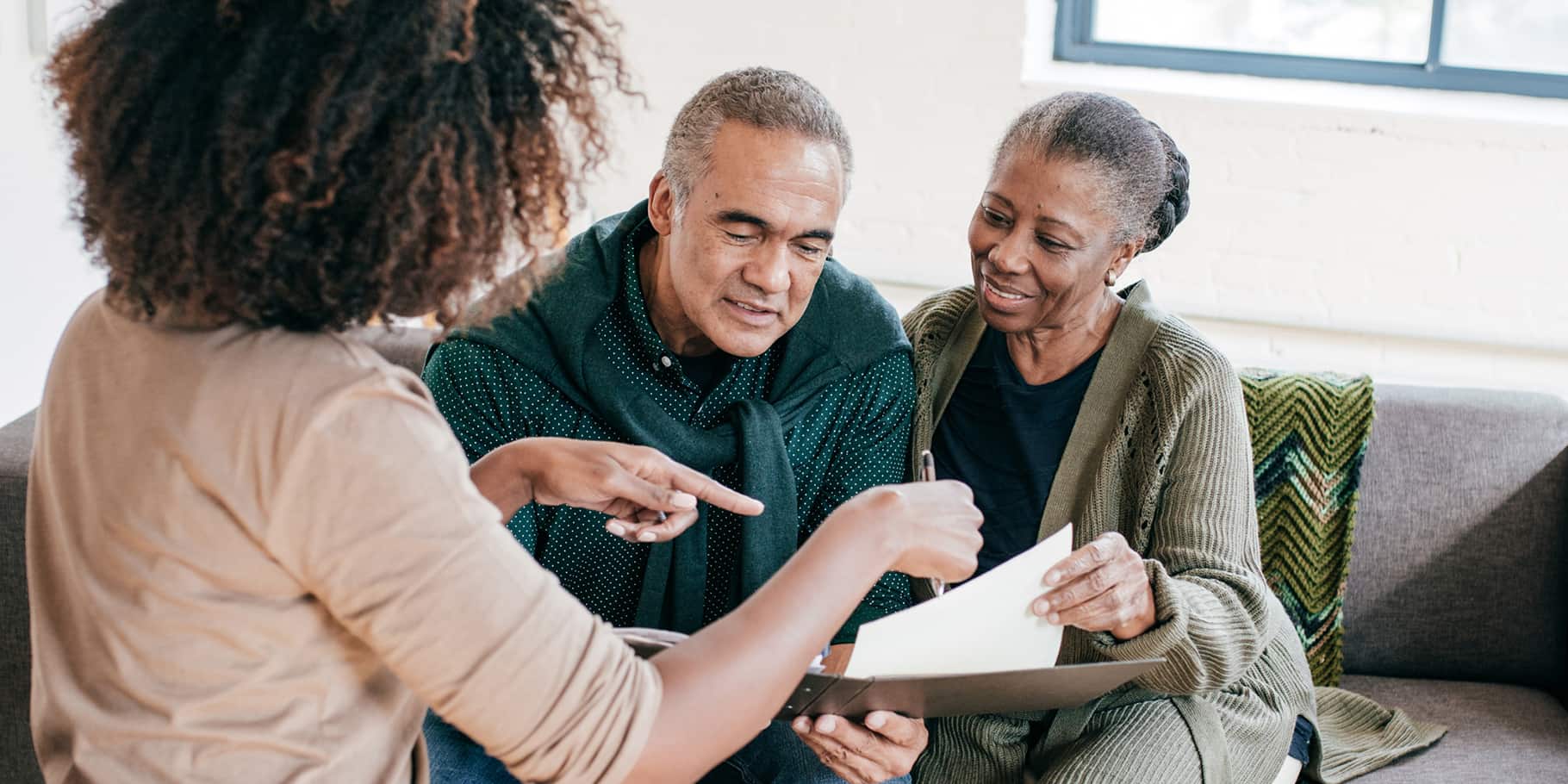 An elderly couple being assisted by a younger woman with documents.
