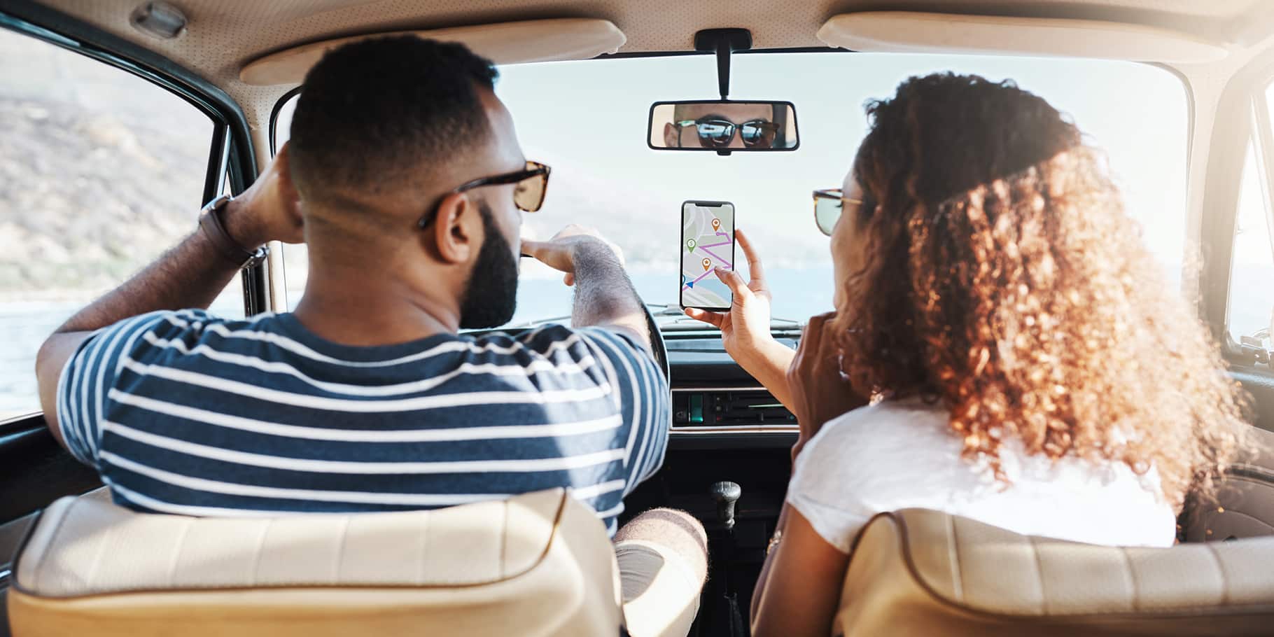 A back-seat view of a young couple driving while looking at a maps app on a smart phone.